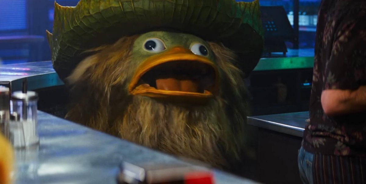 Une capture d'écran tirée du film Detective Pikachu. Un pokemon (je ne me souviens plus de son nom, mais il ressemble à un psykokwak  vert portant un chapeau, ouvre grand le bec.